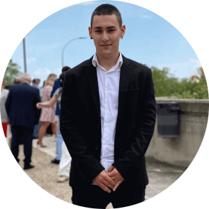 Oskar dressed in a formal attire in what seems to be a family event, outside, in a bodyguard pose while smiling.