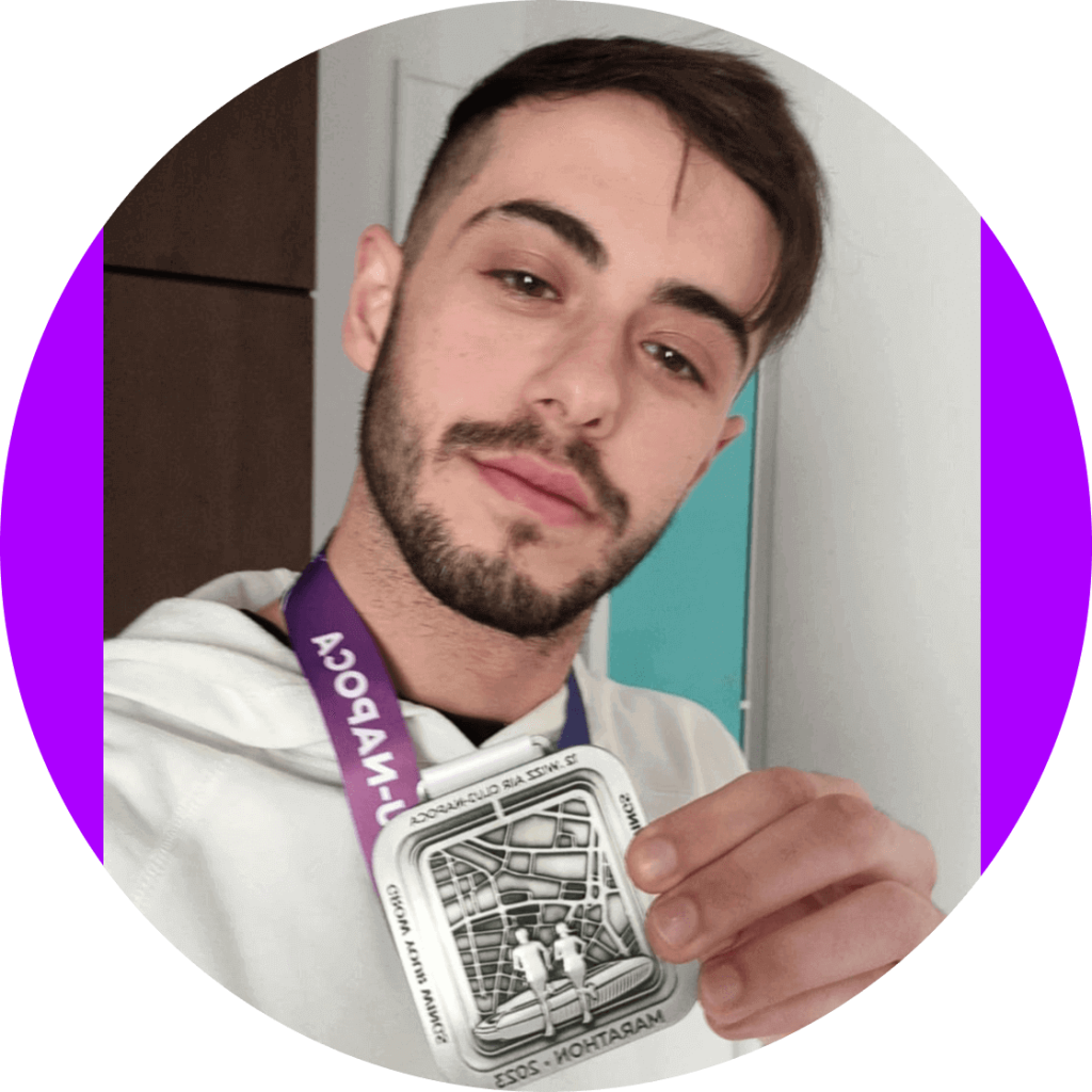 Pablo Escribano holding a medal from a marathon competition in the city of Cluj Napoca, Romania. He is smiling while proudly hoding his medal.